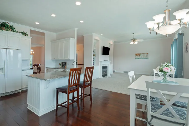 Open-concept layout featuring wood-finish flooring, a kitchen island with stone countertop, white cabinetry, and recessed lighting