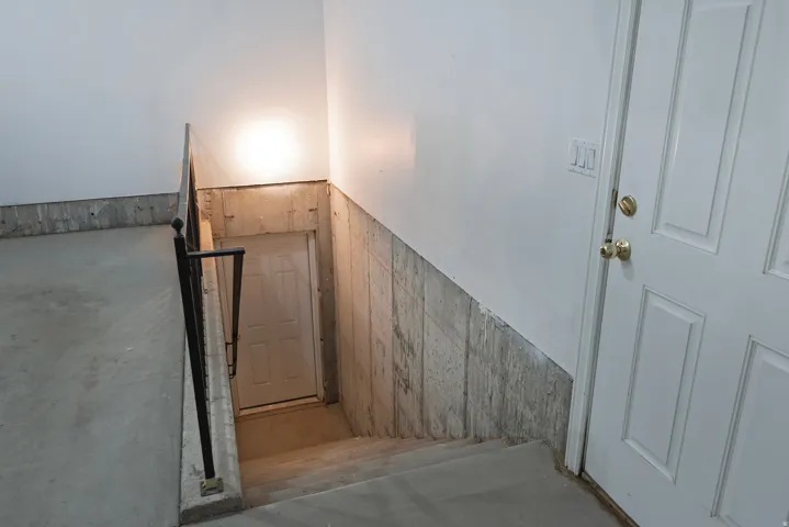 Concrete staircase with a metal handrail, leading to a paneled door