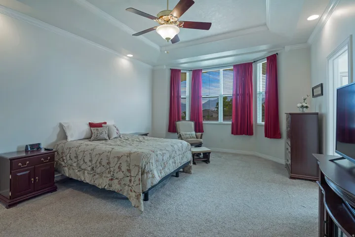 Tray ceiling with crown molding, ceiling fan, recessed lighting, bay window, and carpet flooring