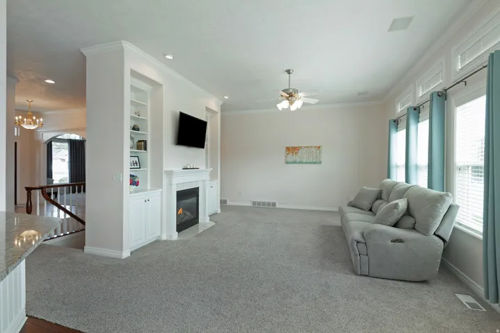 Built-in shelving and cabinetry, fireplace, crown molding, ceiling fan, and multiple windows with blinds