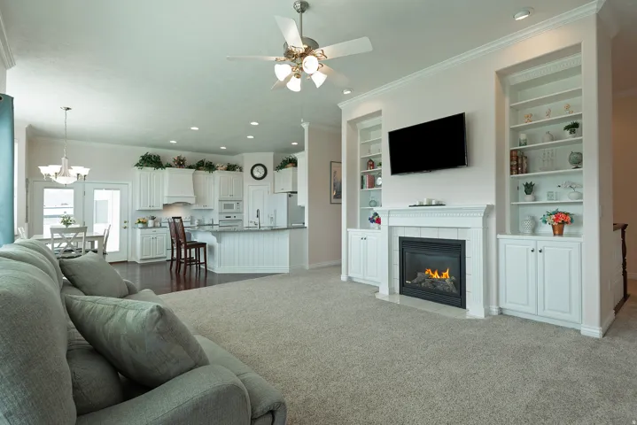 Living area featuring a fireplace with a white mantel, built-in shelving, and a ceiling fan