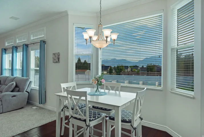 Bay window with expansive mountain scenery, wood-finish flooring, white dining table, and a chandelier with frosted glass shades