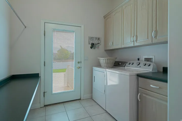 Utility room with tile flooring, built-in upper cabinetry, a long wall-mounted counter, and a glass-paneled exterior door