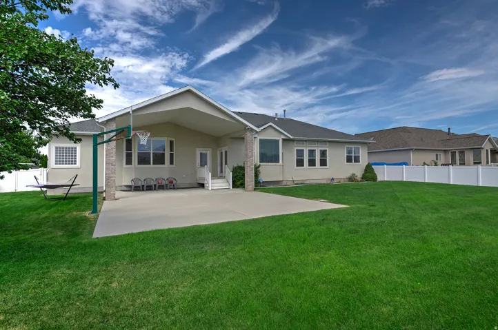 Expansive lawn area, concrete patio, covered outdoor living space, white vinyl fencing, and multiple rear-facing windows