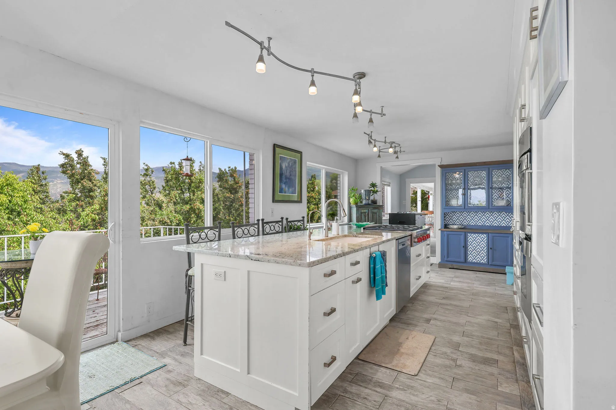 White kitchen island with stone countertop, stainless steel appliances, wood-finish flooring, white cabinetry, and track lighting