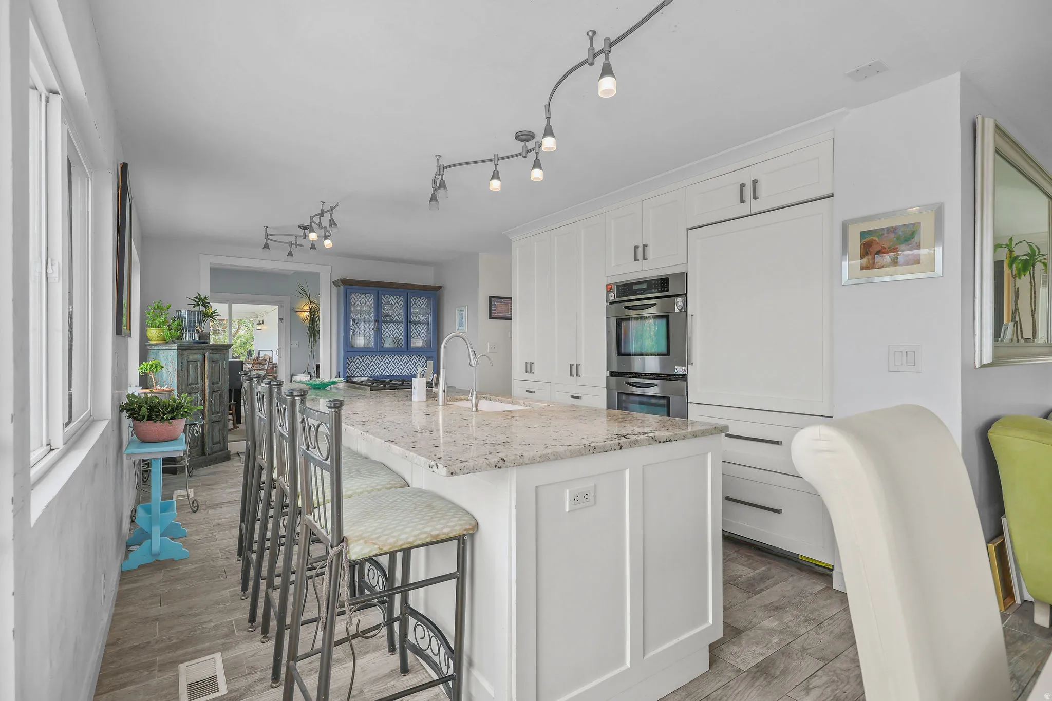 Kitchen featuring white cabinetry, a central island with a light-toned countertop, stainless steel double ovens, and track lighting