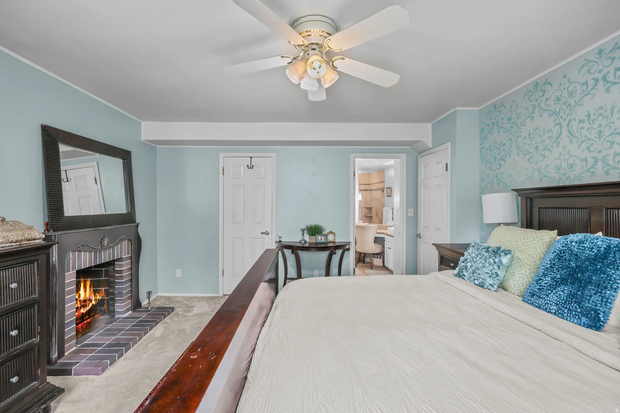 Brick fireplace with wood mantel, ceiling fan with integrated lighting, and patterned accent wall