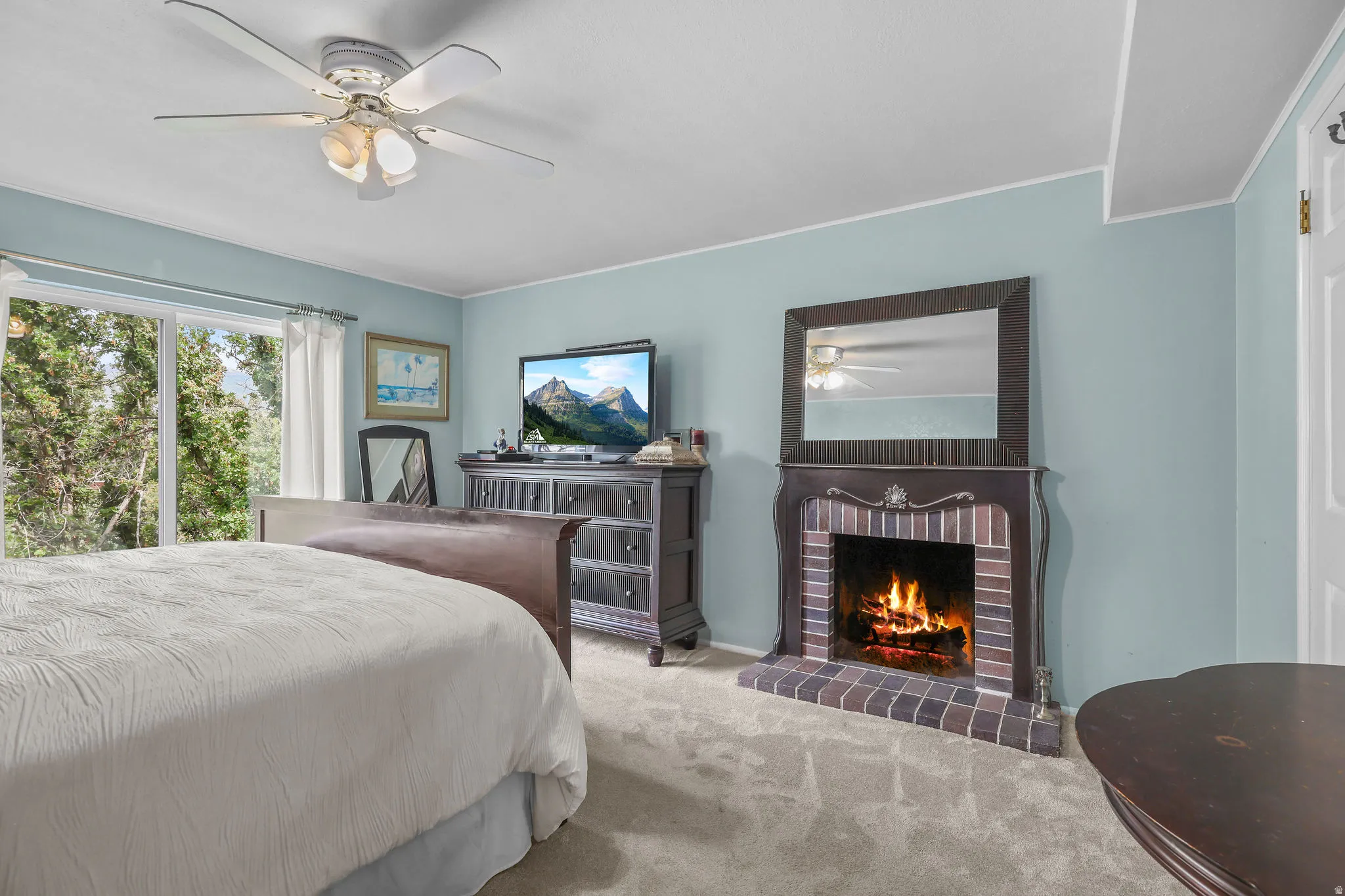 Fireplace with brick surround, ceiling fan with integrated lighting, sliding glass door, and wall-to-wall carpeting
