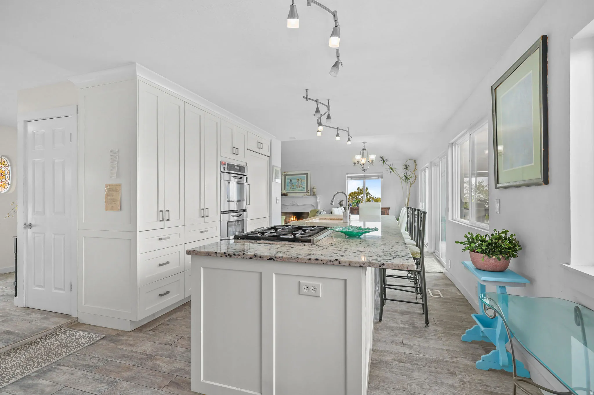 Kitchen featuring extensive white cabinetry, integrated stainless steel double ovens, a center island with a gas cooktop, stone countertops, and plank-style flooring