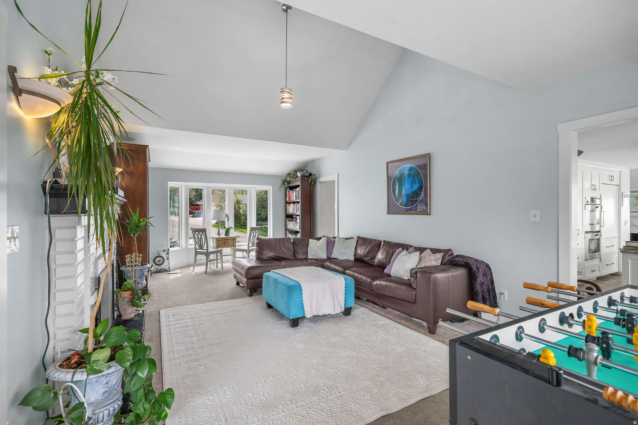Vaulted ceiling with pendant lighting, bay window, and white brick fireplace