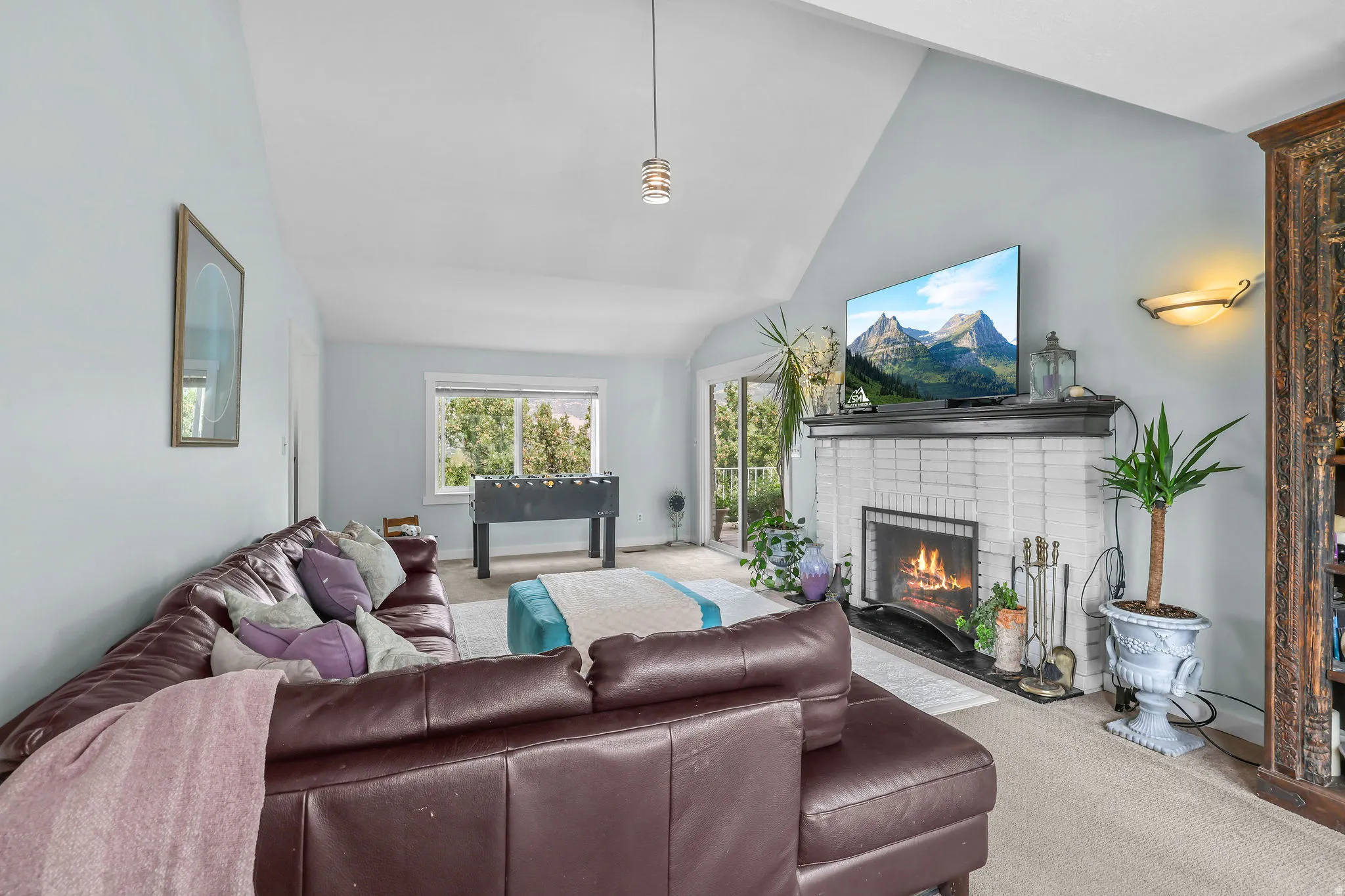 Vaulted ceiling enhancing vertical space, white brick fireplace with a dark mantel, glass sliding door, and wall-mounted lighting fixture