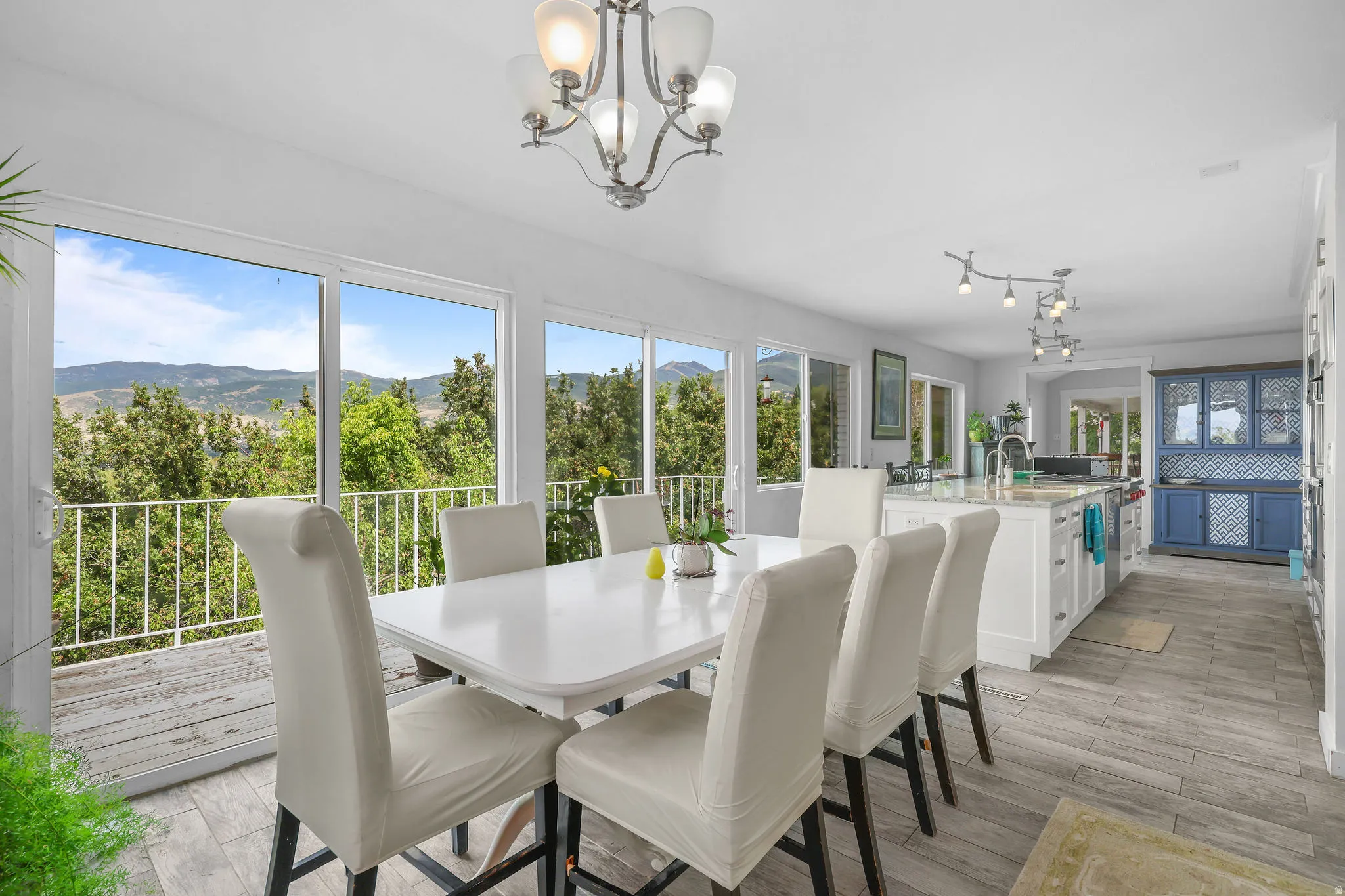 Open-concept living area with large glass sliding doors, wood-finish flooring, a contemporary chandelier, a kitchen island with built-in cabinetry, and a distinct blue built-in hutch