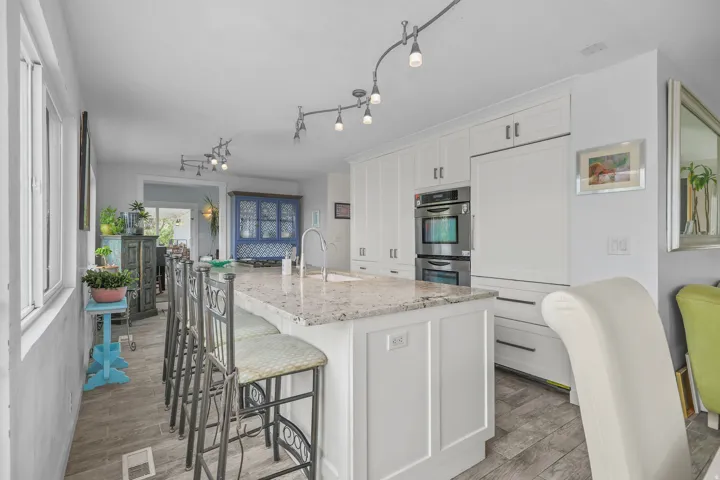 Kitchen featuring white cabinetry, a central island with a light-toned countertop, stainless steel double ovens, and track lighting