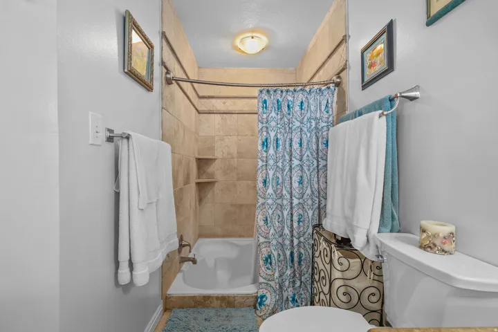 Full-height tiled shower surround with built-in shelving, white bathtub, and light gray wall paint