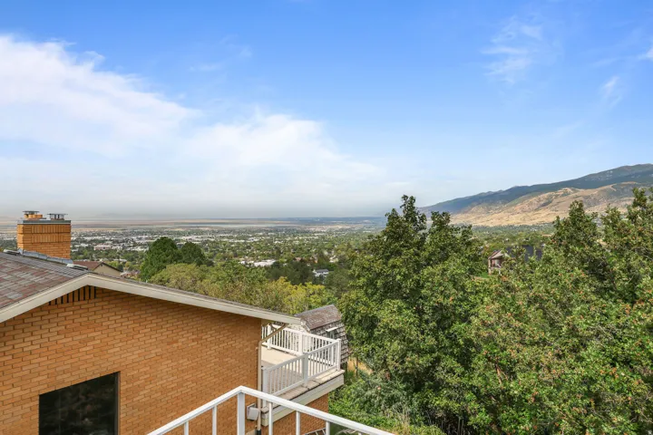 Expansive city and mountain backdrop, mature trees, brick exterior, white balcony railing, and a shingle roof