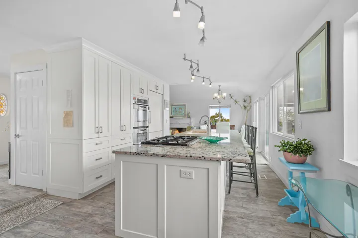 Kitchen featuring extensive white cabinetry, integrated stainless steel double ovens, a center island with a gas cooktop, stone countertops, and plank-style flooring