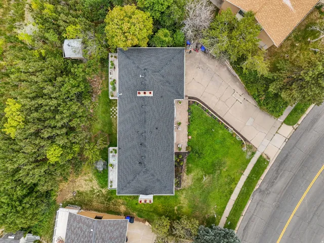 Aerial view showcasing this residence featuring a newly installed asphalt roof, manicured lawn with mature landscaping, paved driveway, and direct street access