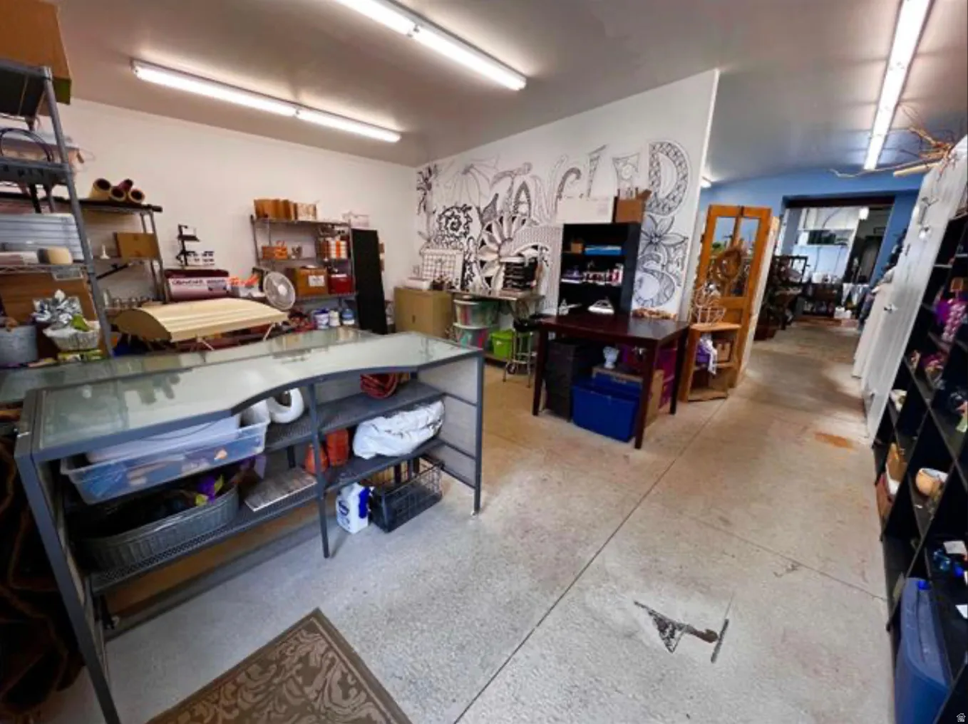 Concrete flooring, white walls, exposed fluorescent lighting, built-in shelving, and a wood-finish door frame