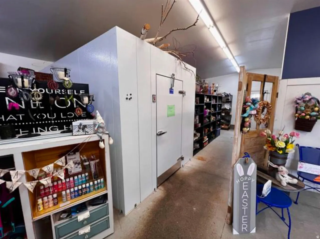 Walk-in cooler, fluorescent lighting, built-in shelving, painted concrete flooring, and a single wooden door