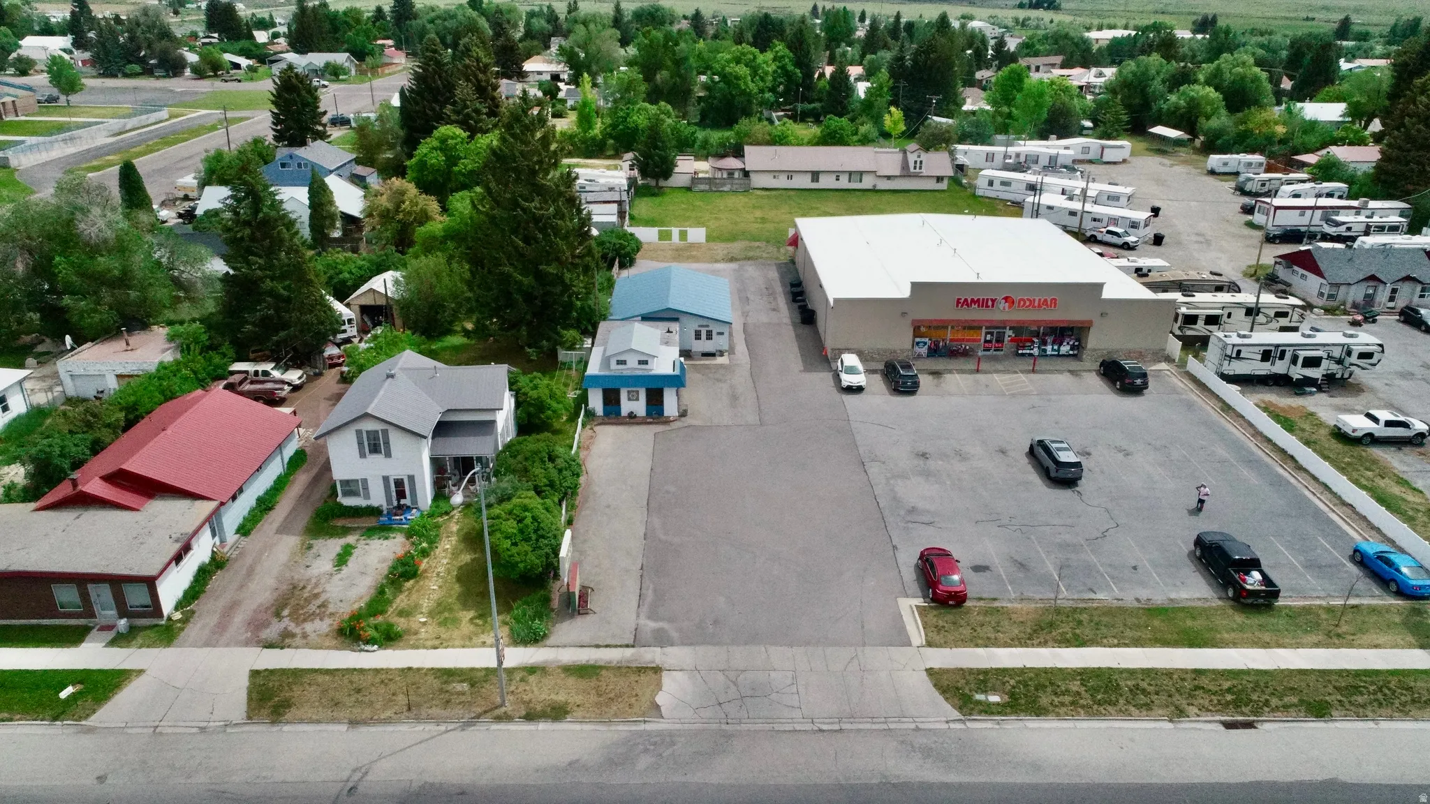 Expansive paved parking lot, commercial building with prominent signage, adjacent residential properties, and mature trees surrounding the area
