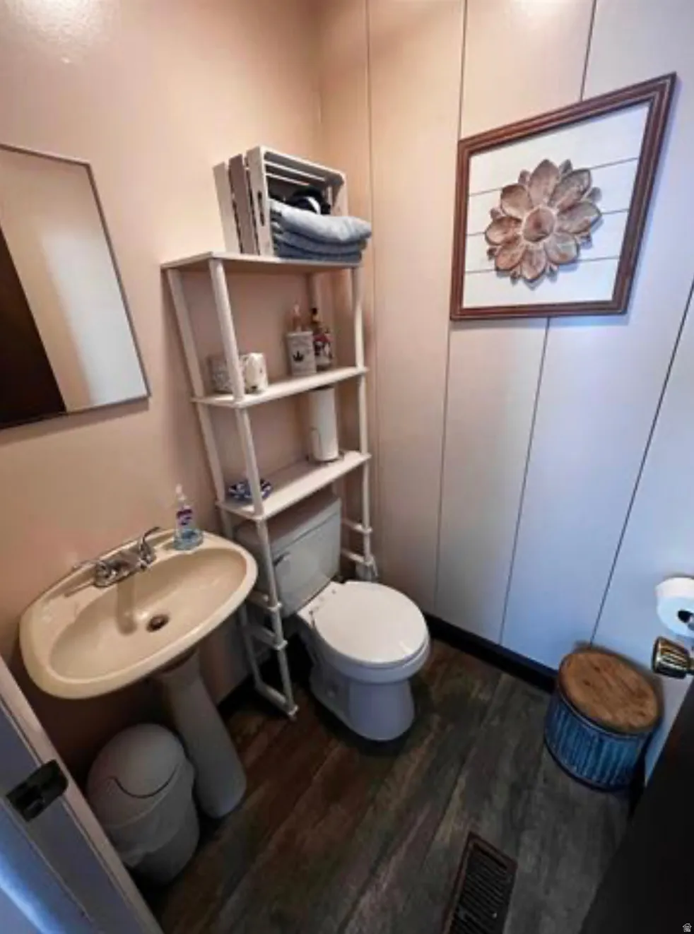 Pedestal sink with chrome faucet, toilet with white ceramic bowl, wood-finish flooring, and light-colored wall panels
