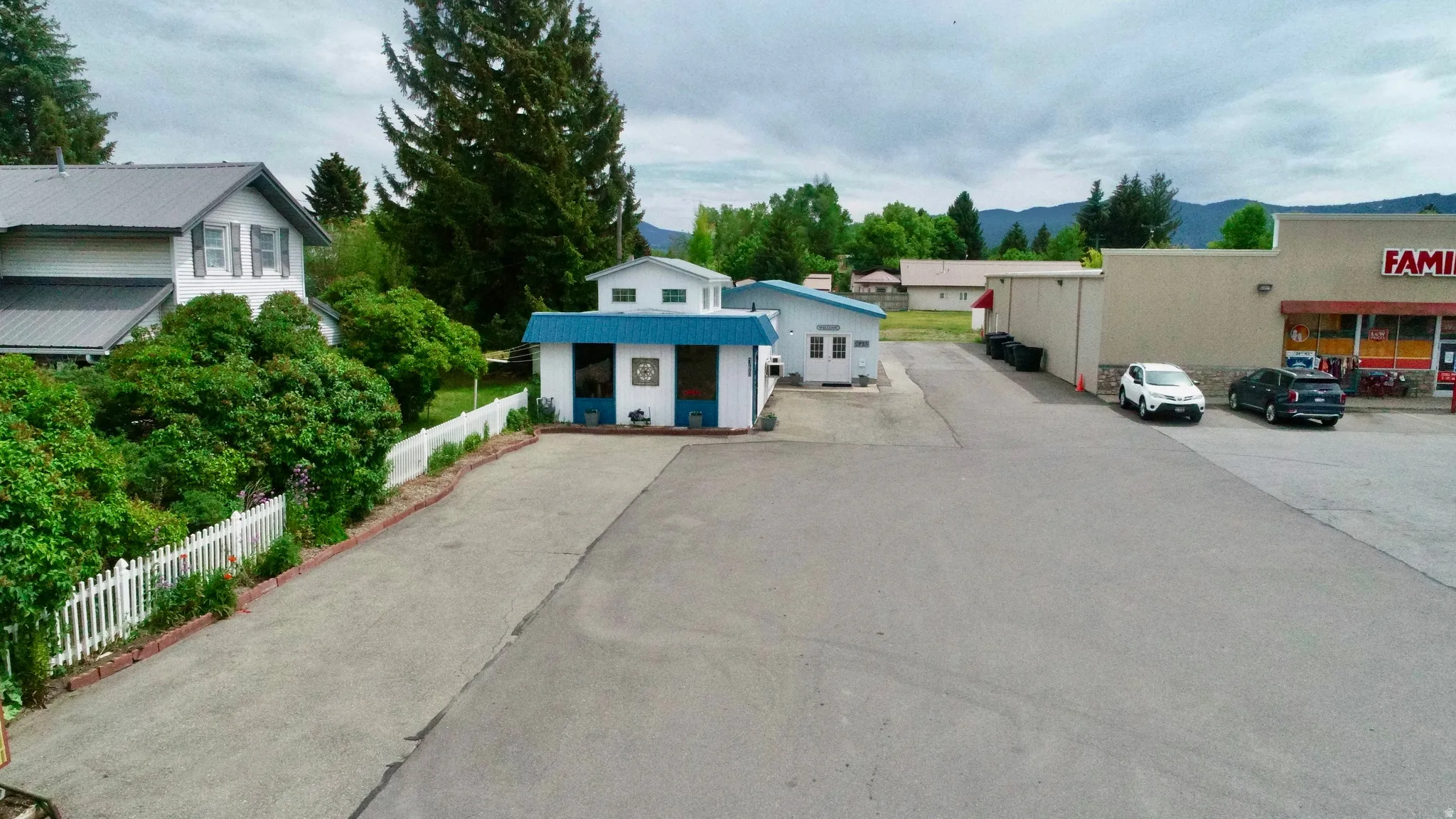 Paved parking area with white picket fencing, mature trees, and a mountain backdrop