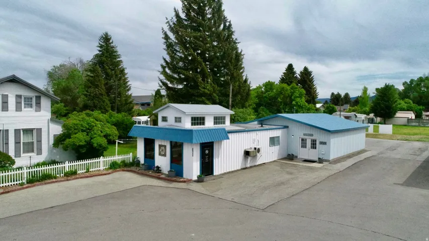 Expansive paved parking area, white siding exterior, blue metal roofing, front entrance with double doors, and a white picket fence