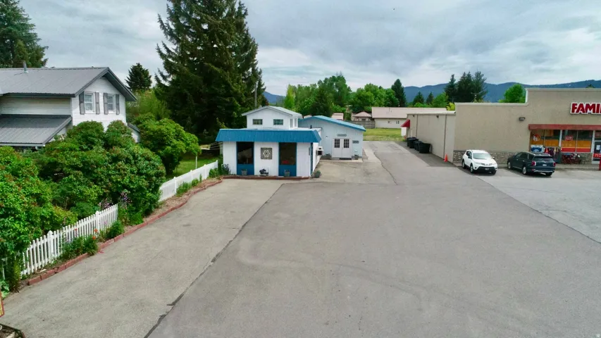 Paved parking area with white picket fencing, mature trees, and a mountain backdrop
