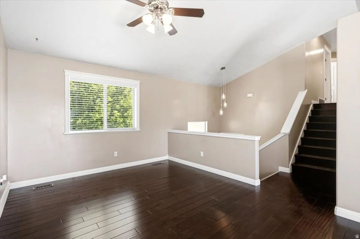 Vaulted ceiling with a ceiling fan, dark wood-finish flooring, staircase with dark treads, and a window with blinds