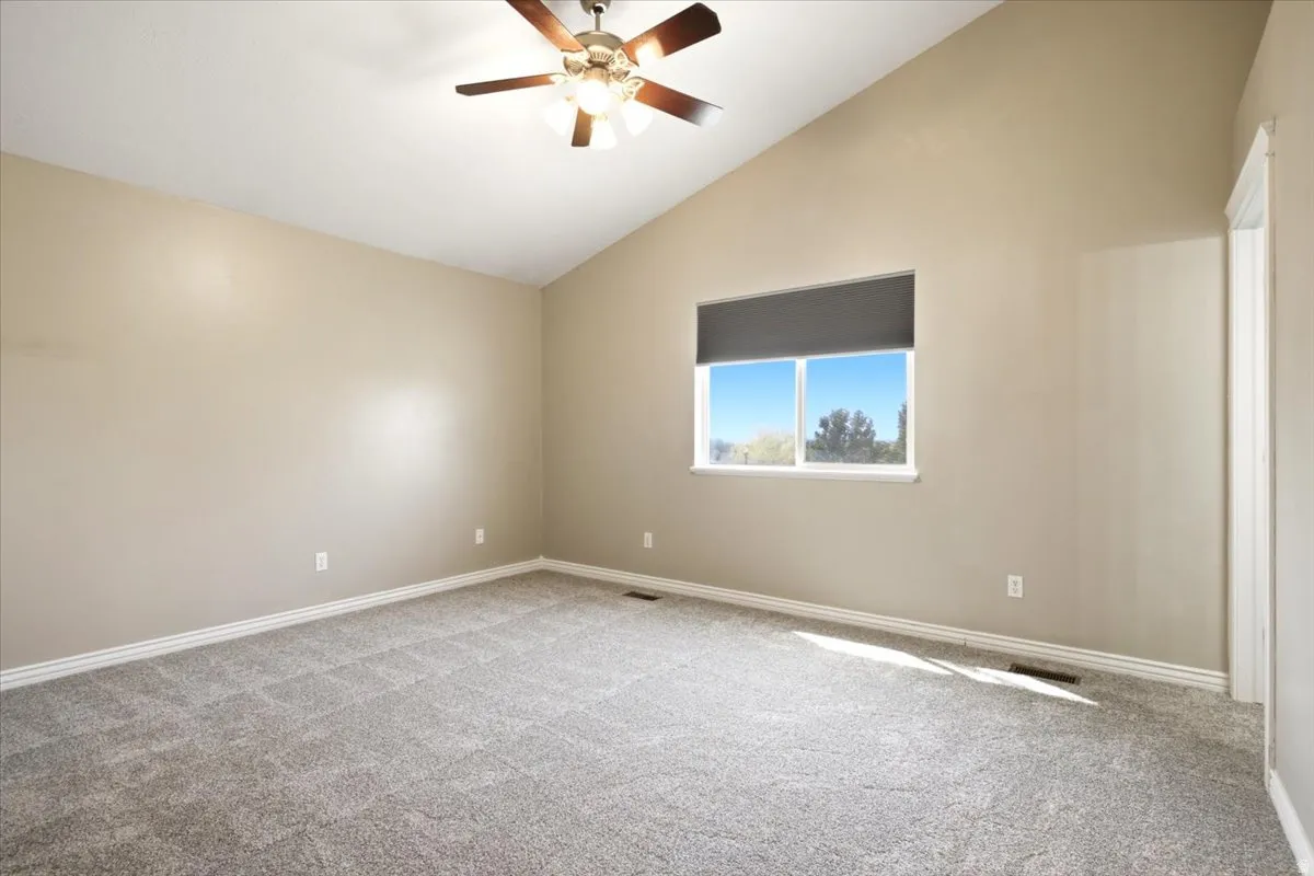 Vaulted ceiling with an attached ceiling fan, neutral carpet flooring, and a window with roller shade