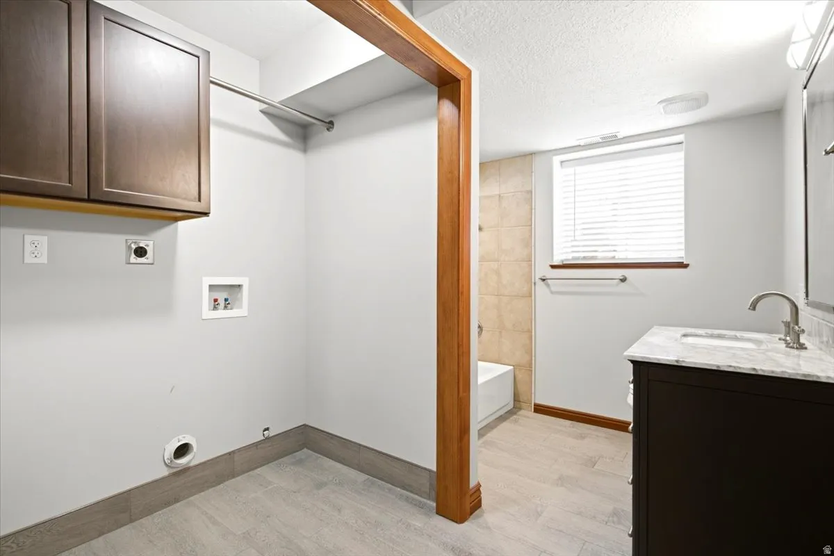 Wood-finish flooring, dark wood cabinetry, white marble-finish countertop, and tiled shower surround