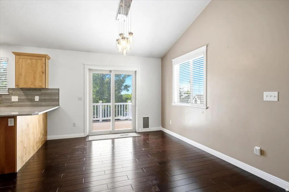 Vaulted ceiling, wood-finish flooring, sliding glass door, contemporary pendant light fixture, and a kitchen peninsula with a tile backsplash