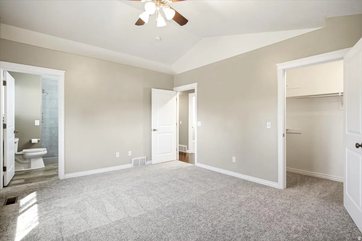 Vaulted ceiling with ceiling fan, light gray carpeting, neutral wall color, white trim, and a walk-in closet