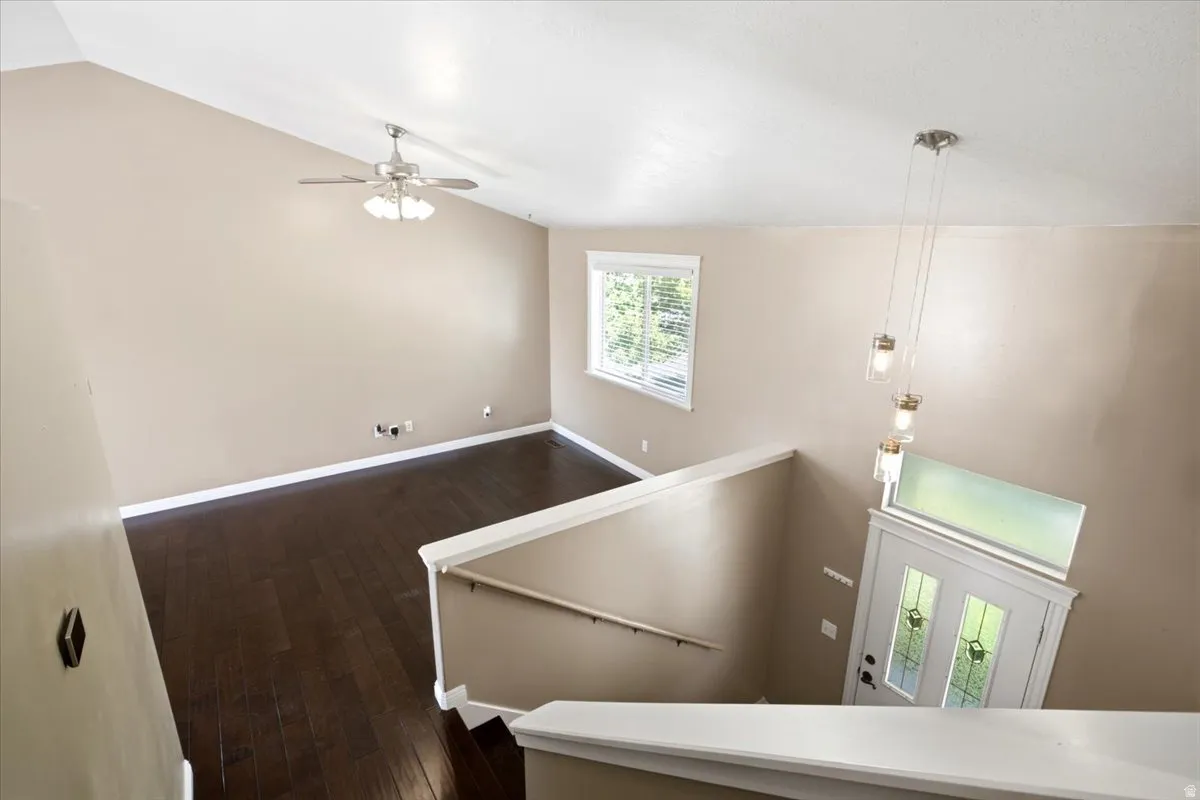 Vaulted ceiling with a ceiling fan, dark wood-finish flooring, a window with blinds, and a white entry door with decorative glass inserts