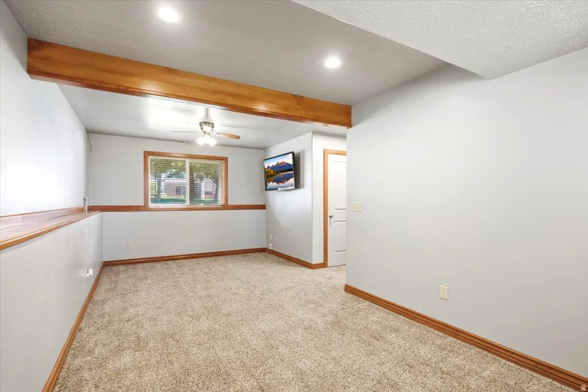 Recessed lighting, wood-finish ceiling beam, ceiling fan, wood-trim window, and plush carpet flooring