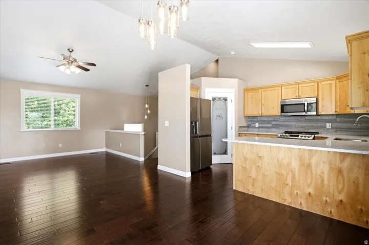 Vaulted ceiling, dark wood-finish flooring, light wood cabinetry, stainless steel appliances, and a kitchen island with a light-colored countertop