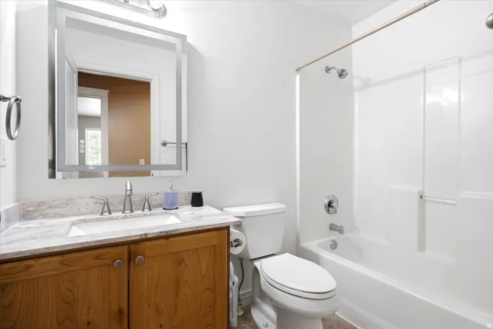 Wood-finish vanity with a rectangular undermount sink, stone-look countertop, and satin nickel faucet