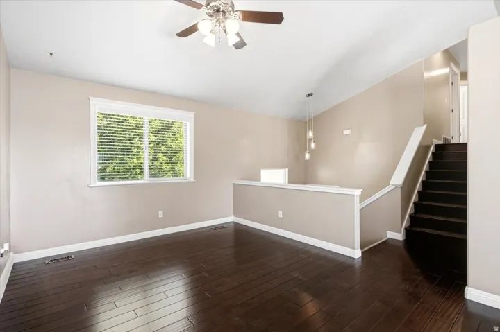 Vaulted ceiling with a ceiling fan, dark wood-finish flooring, staircase with dark treads, and a window with blinds