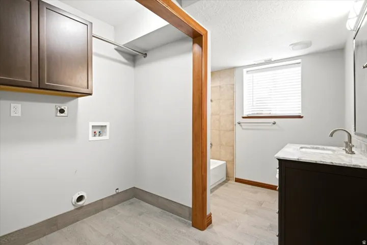Wood-finish flooring, dark wood cabinetry, white marble-finish countertop, and tiled shower surround