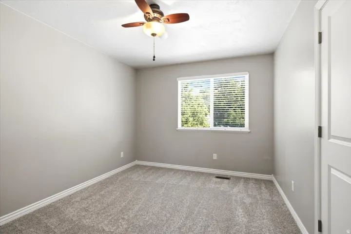 Neutral-toned walls, textured gray carpeting, white window blinds, and a ceiling fan with light fixture