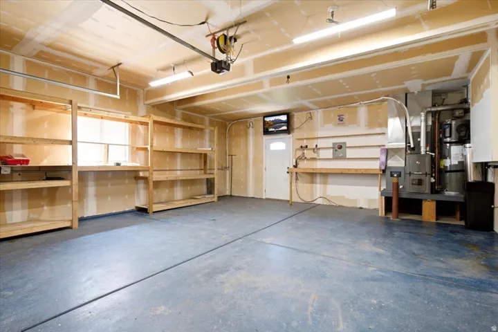 Spacious garage with a concrete floor, built-in wooden shelving, and fluorescent lighting