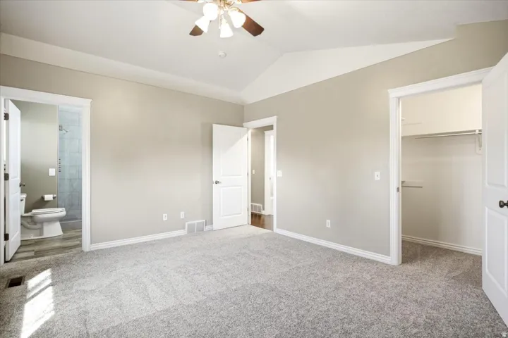 Vaulted ceiling with ceiling fan, light gray carpeting, neutral wall color, white trim, and a walk-in closet