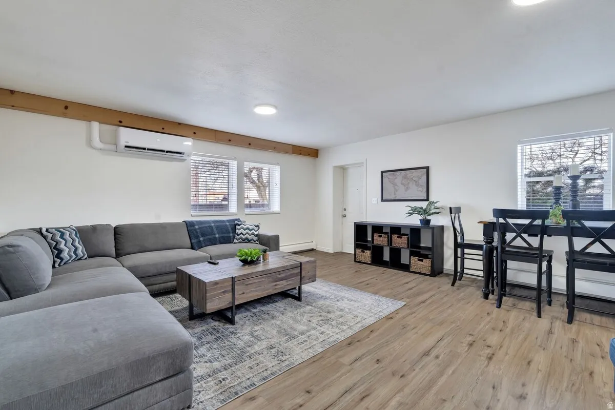 Wood-finish flooring, white walls, exposed wood beam, recessed lighting, and a wall-mounted mini-split system