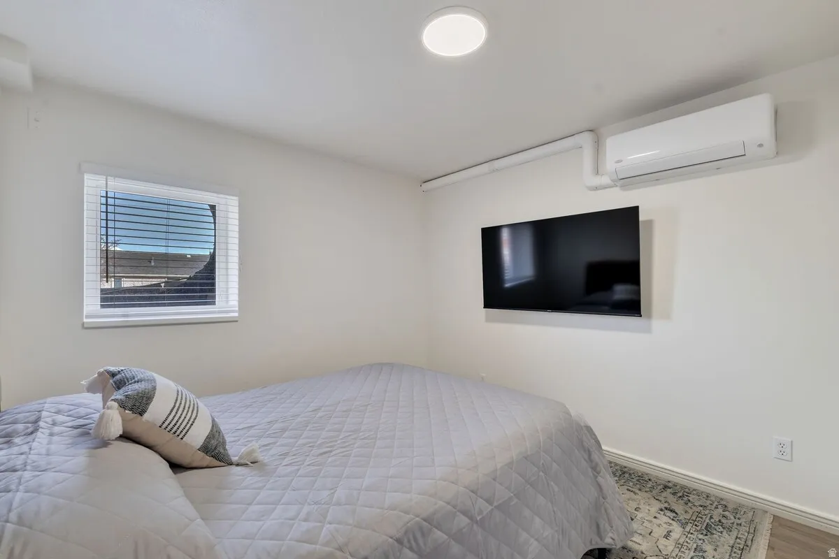 Wall-mounted air conditioning unit, ceiling-mounted light fixture, window with blinds, and light-toned flooring