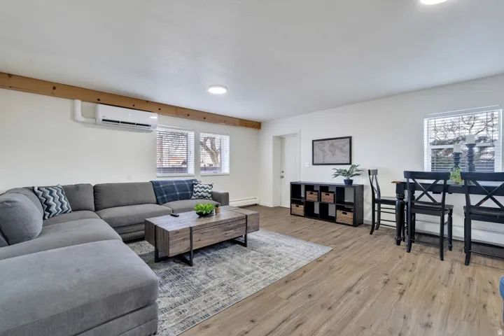 Wood-finish flooring, white walls, exposed wood beam, recessed lighting, and a wall-mounted mini-split system