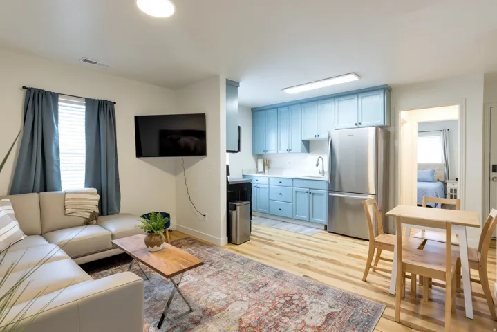 Open-concept living area featuring light wood-finish flooring, a kitchen with light blue cabinetry, stainless steel appliances, and a dining area with a light wood table