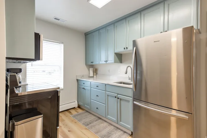 Kitchen featuring light blue cabinetry, stainless steel refrigerator, undermount sink, and light-toned wood-finish flooring