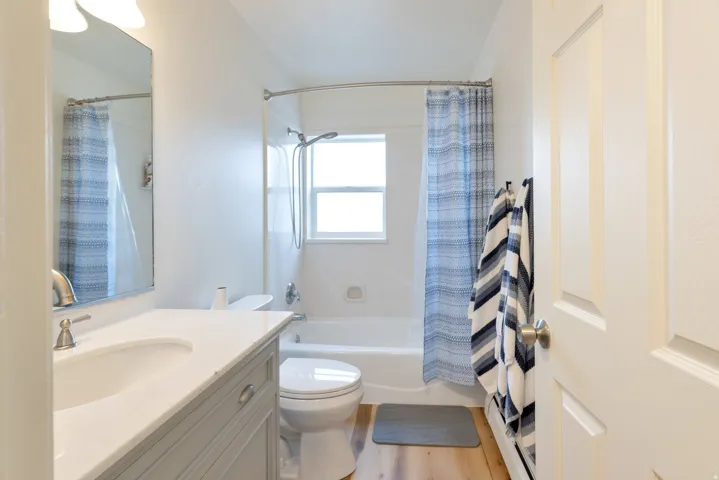Bathroom featuring a single vanity with an integrated sink, a built-in tub with a shower, a window, and wood-finish flooring