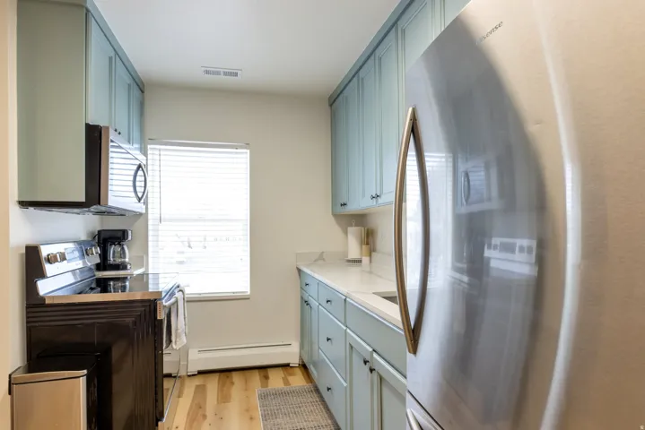 Kitchen featuring painted cabinetry, light-toned countertops, wood-finish flooring, and stainless steel appliances including a refrigerator, range, and microwave