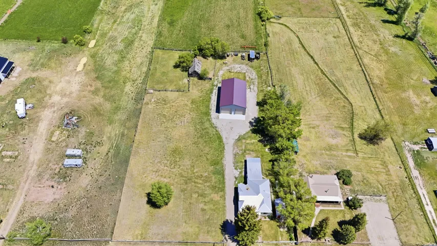 Expansive property featuring a primary residence with a light-colored roof, a separate structure with a purple roof, and surrounding green fields